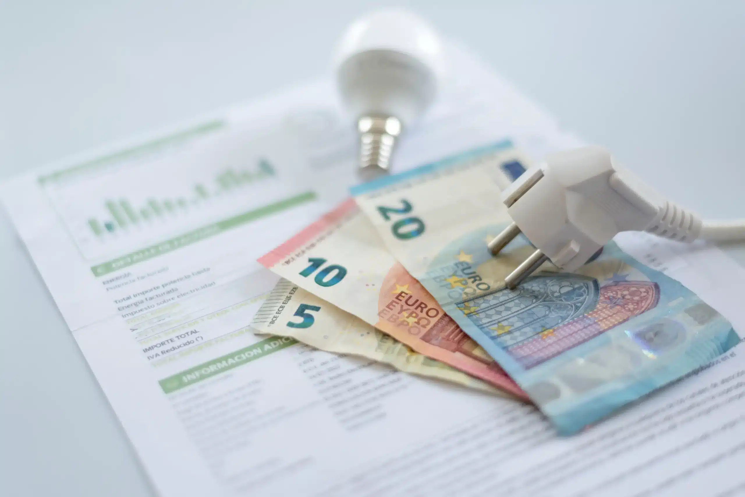 Factura de electricidad cara con billetes de euro y bombilla, representando el ahorro en la tarifa de luz